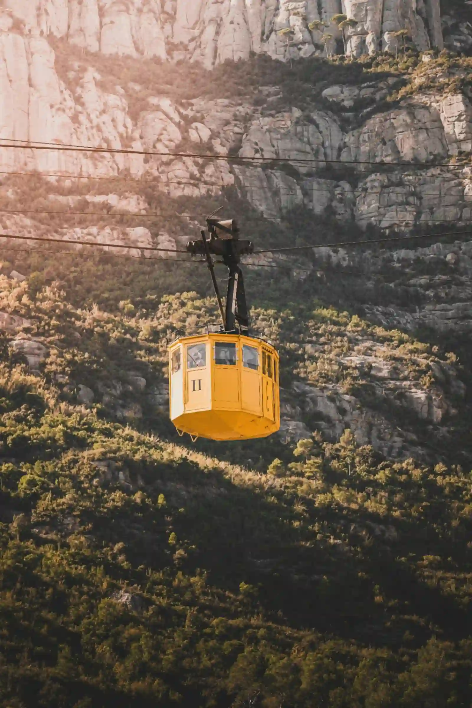 Historic yellow Montserrat aeri cable car ascending the dramatic serrated rock cliffs of the Catalan mountain at golden hour