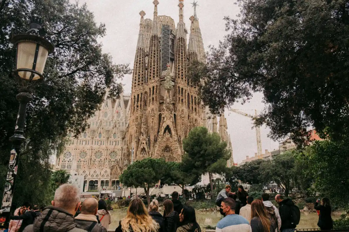 Sagrada Familia basilica facade in Barcelona framed by trees with visitors gathered in the foreground