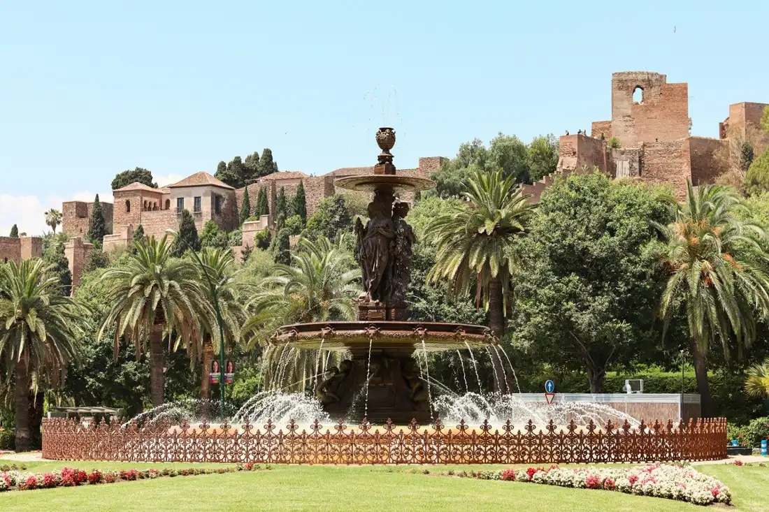 The Alcazaba fortress of Malaga rising above palm trees and the historic gardens fountain