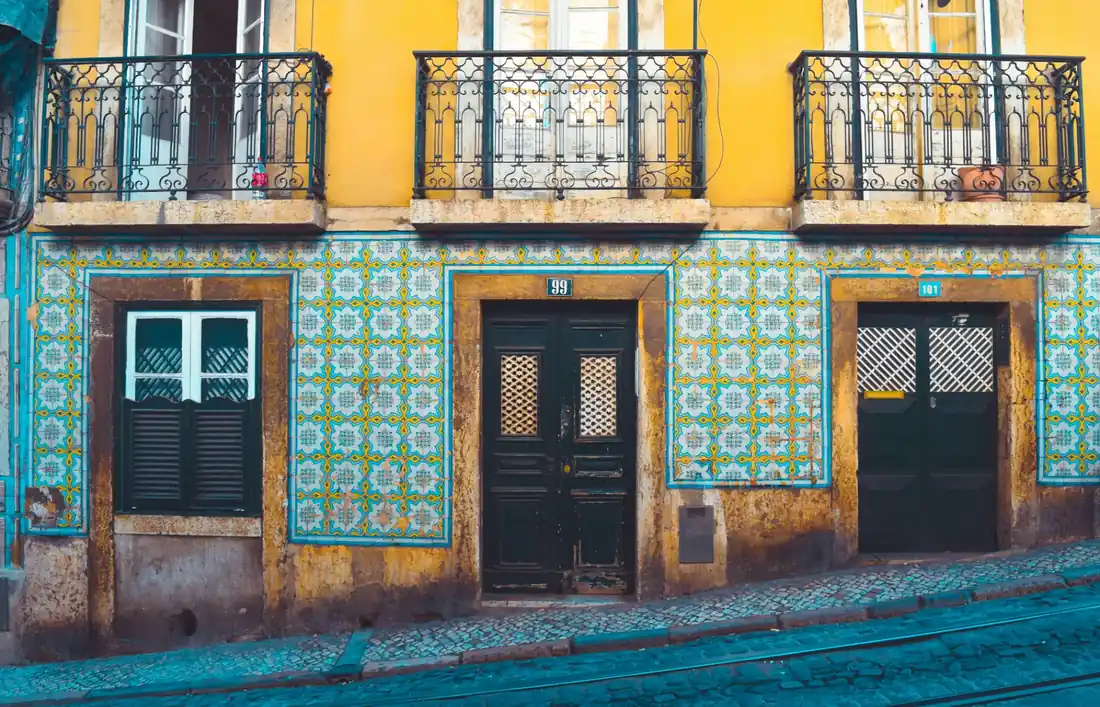 Traditional Lisbon facade covered in blue and yellow azulejo tiles with wrought iron balconies in the Alfama district