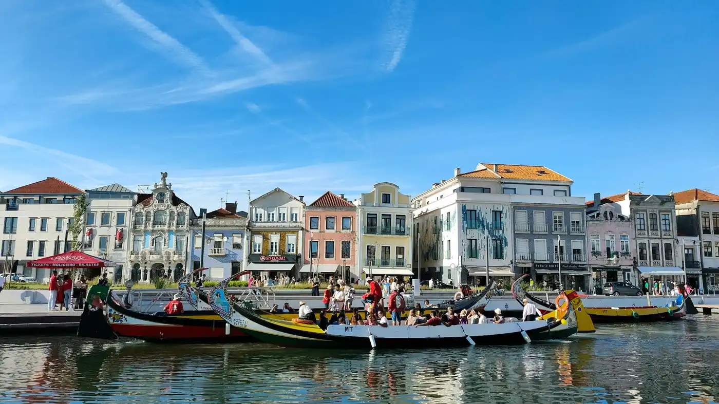Colorful traditional moliceiro boats along the Aveiro canal with pastel art nouveau buildings under a cloudy sky