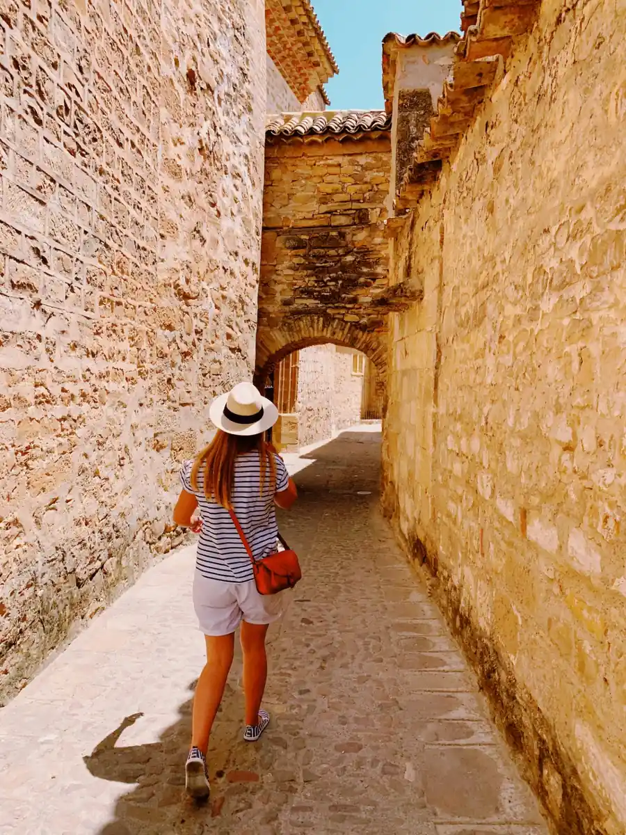 Traveler walking through a narrow historic stone alley in Baeza, Andalusia, beneath an arched Renaissance passageway