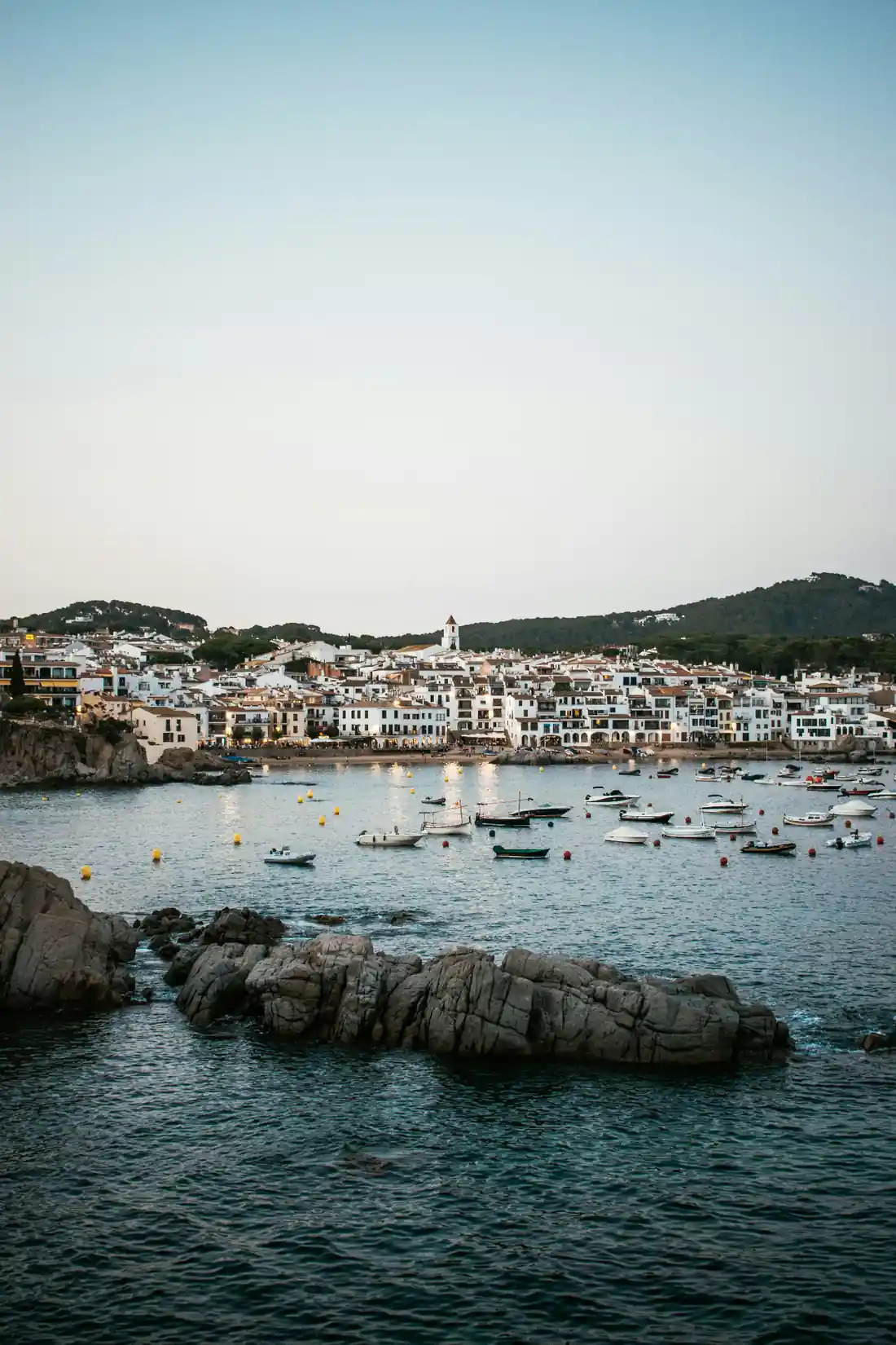 Whitewashed houses of Calella de Palafrugell fishing village at dusk with boats anchored in the Costa Brava bay