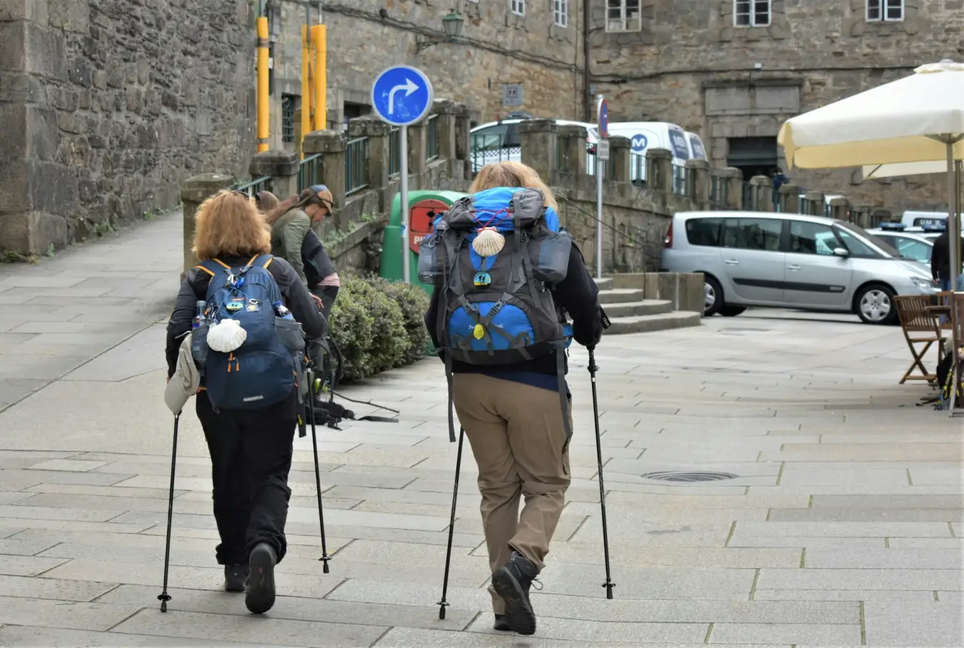 Dos peregrinos con mochilas y vieiras caminando por las últimas calles del Camino de Santiago
