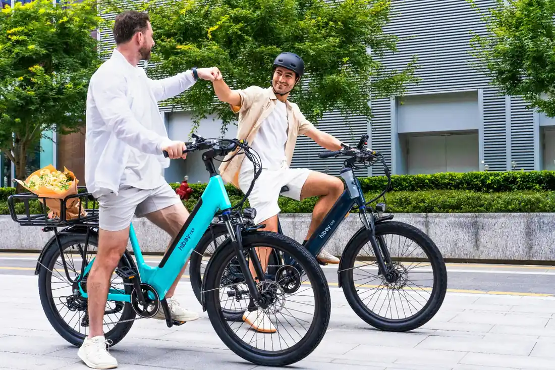 Two friends on e-bikes greeting each other with a fist bump on a city promenade during a guided tour