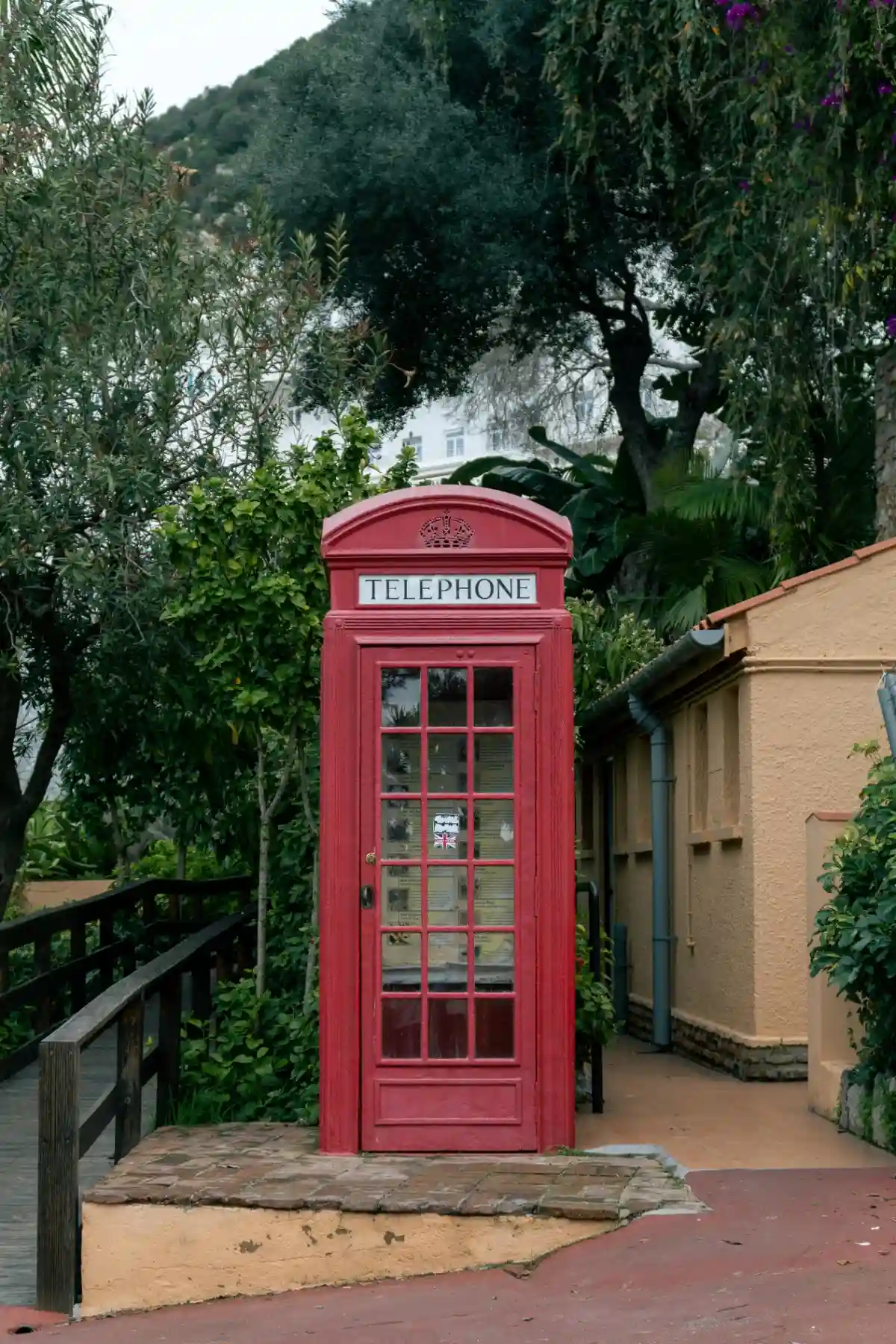 Classic red British telephone booth on a lush green street in Gibraltar with the Rock in the background