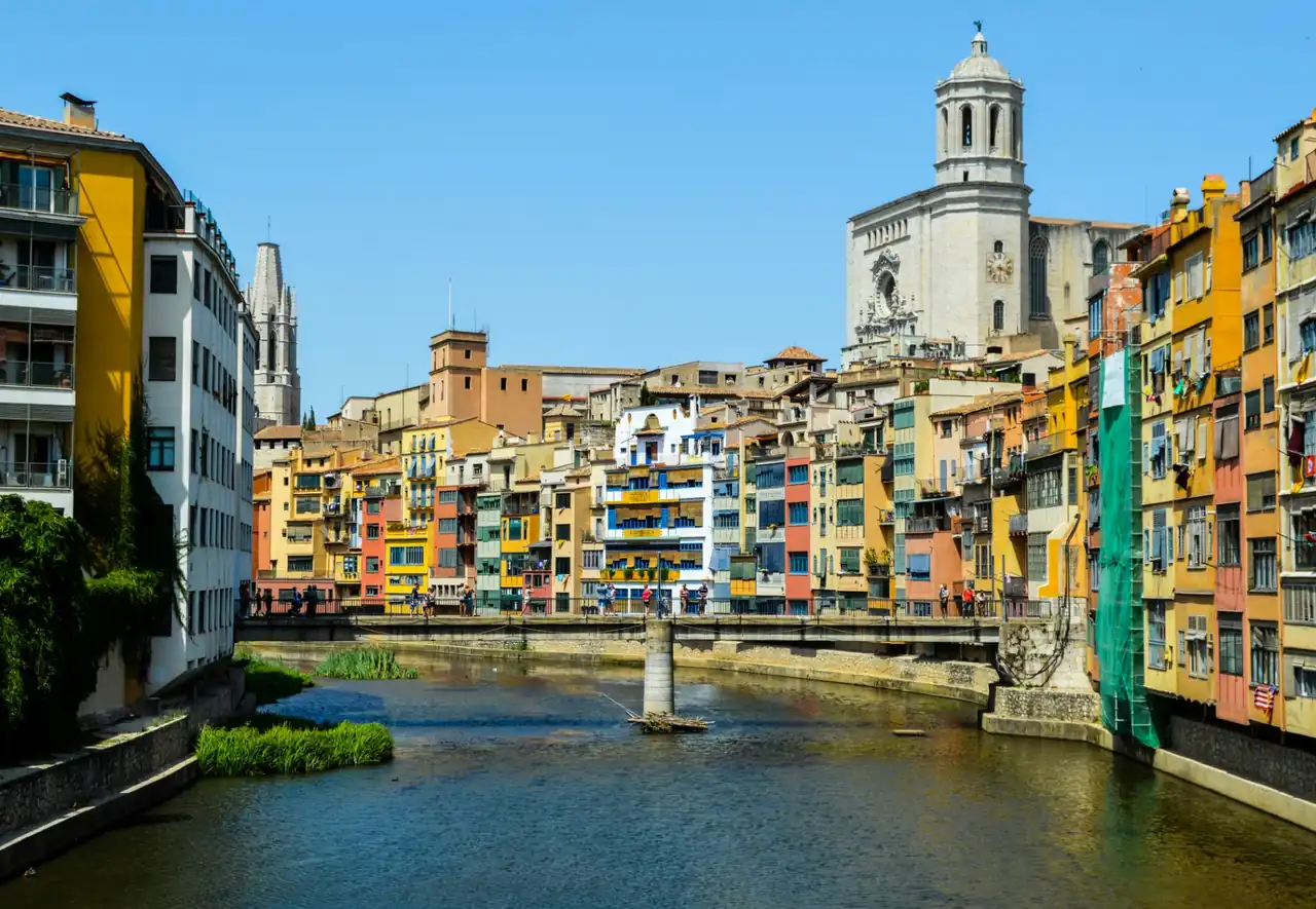 Colorful houses along the Onyar River in Girona with the cathedral rising above the historic center