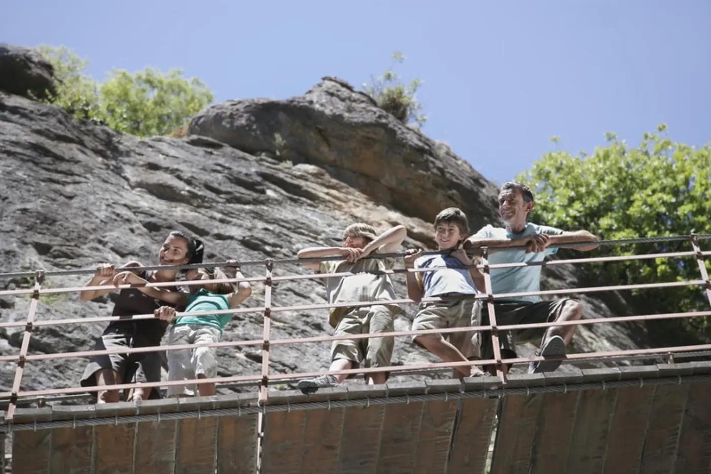 Hiker crossing a suspension bridge over the turquoise Monachil River gorge in Los Cahorros