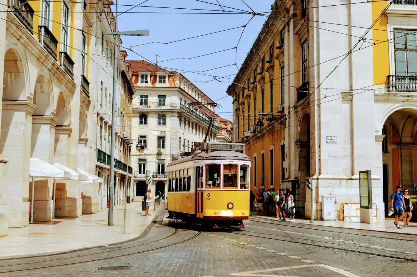 Iconic yellow Lisbon tram number 25 passing through Praça do Comércio between historic arcaded buildings