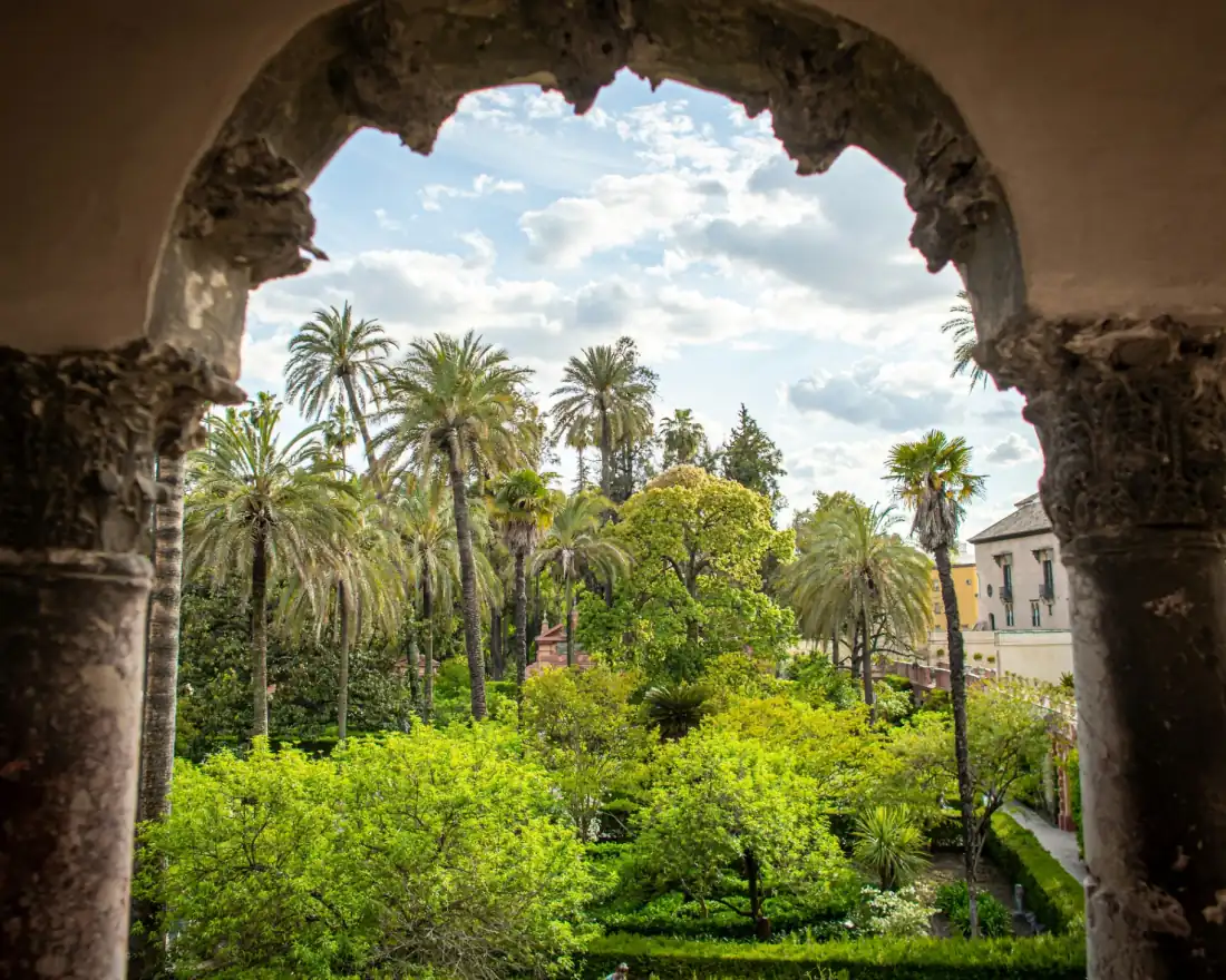 View of the Royal Alcázar gardens in Seville framed by a Mudéjar stone arch