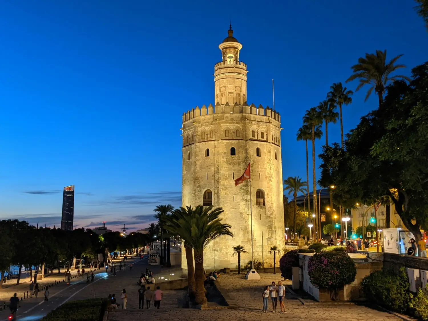 The illuminated Torre del Oro standing along the Guadalquivir riverside in Seville at twilight with palm trees