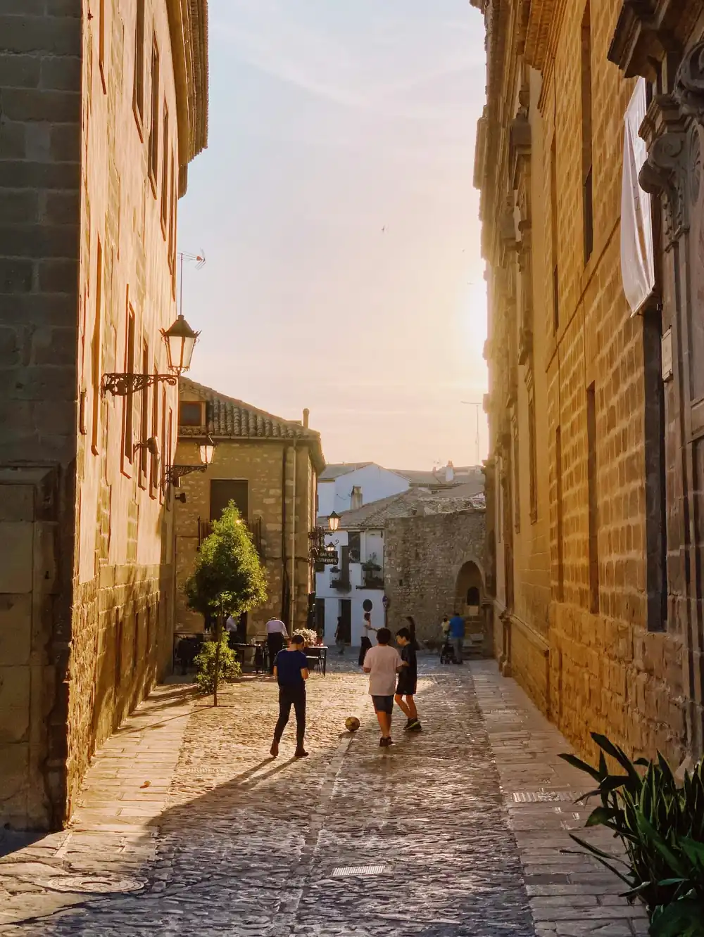 Golden evening light pouring down a quiet cobbled street in Úbeda's Renaissance old town, framed by honey-stone palaces